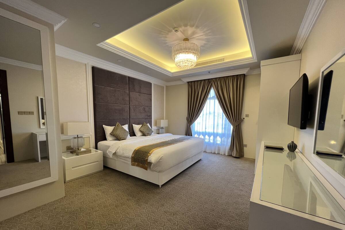 A modern hotel room with a large bed, a vanity with a mirror, a chandelier, and a television on the wall.