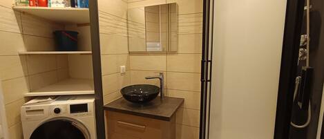 A compact bathroom with a washing machine, a sink with a black basin, and a mirror above it.