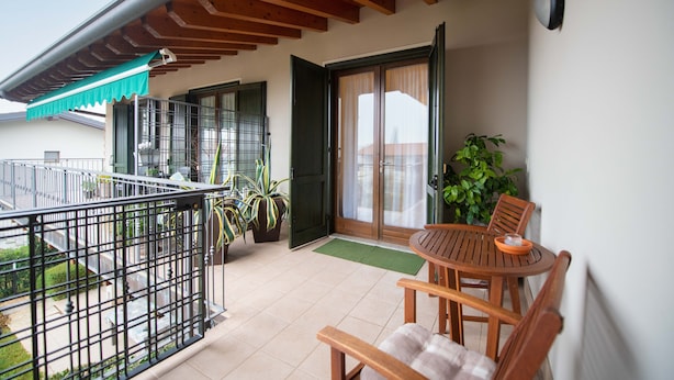 A balcony with a wooden table and chairs, a potted plant, and a sliding glass door. - Appartamento Maria Cristina (Polpenazze del Garda)