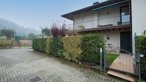 A two-story house with a paved driveway, a balcony with a railing, and a green door. - Appartamento Maria Cristina (Polpenazze del Garda)