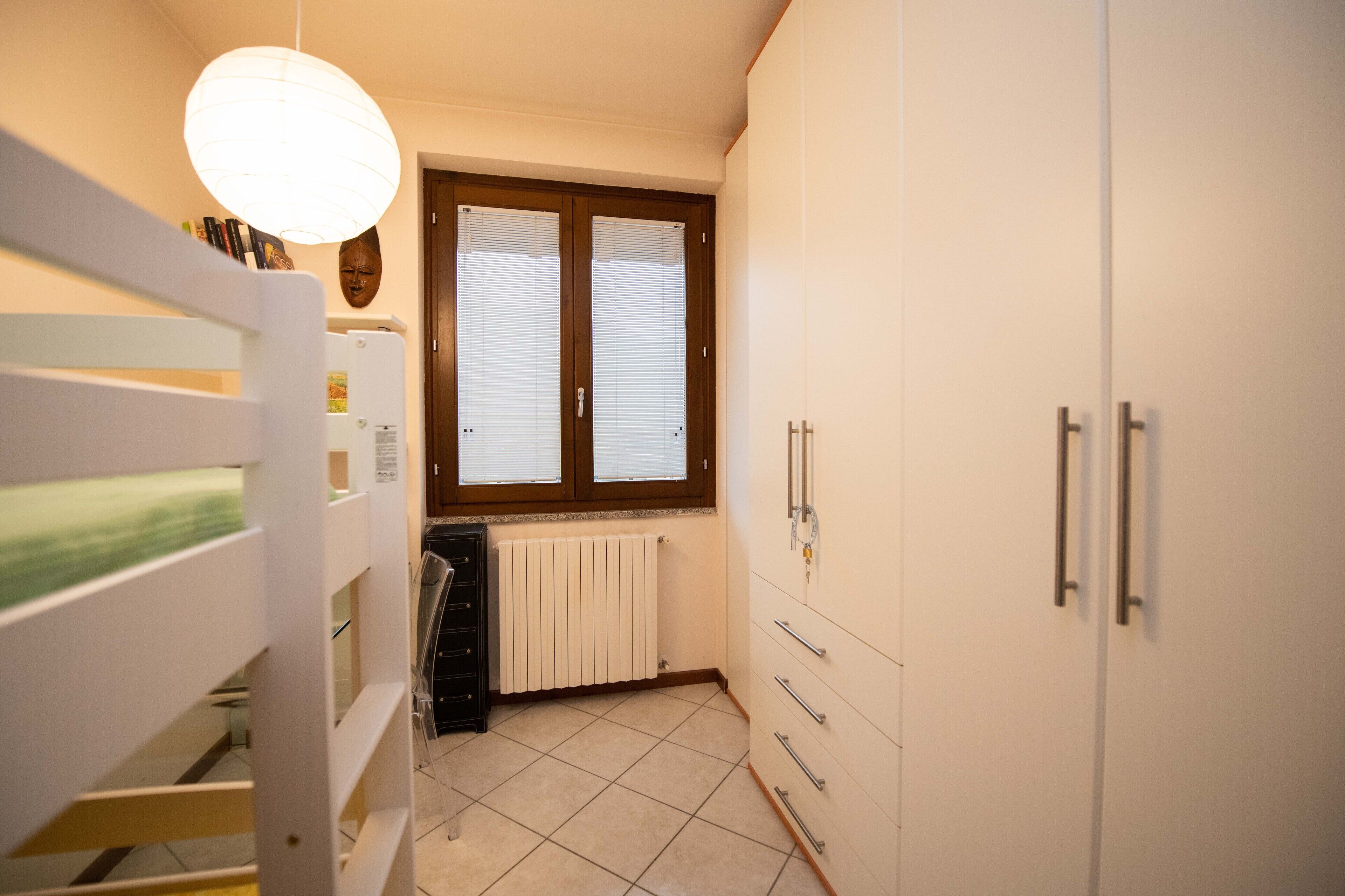 Una camera da letto con un letto a castello, un armadio, un termosifone e una finestra con persiane.