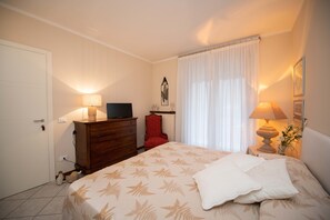 Une chambre à coucher avec un lit, une commode, un téléviseur, une chaise et une fenêtre avec des rideaux.