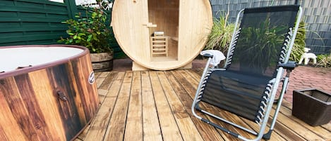 Um deck de madeira com sauna, uma espreguiçadeira e uma banheira de hidromassagem.