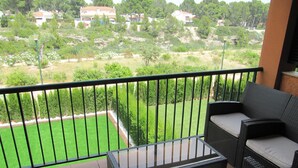 Un balcón con mobiliario de mimbre y vistas a un césped verde y casas a lo lejos.