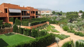 Un edificio moderno con techo plano, varios balcones y un jardín bien cuidado con diferentes plantas y un sendero.