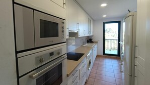 Una cocina compacta con gabinetes blancos, horno empotrado, microondas y lavadora.