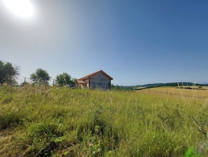 A rural house with a red roof, surrounded by tall grass and fields. - Pretty wooden house with large enclosed garden. (Lafage)