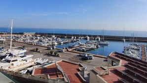 A marina with numerous boats docked, a clear blue sky, and a calm sea in the background.