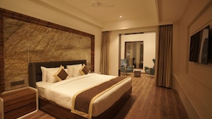 Una habitación de hotel moderna con una cama grande, suelo de madera, una pared decorativa de mármol, un televisor de pantalla plana y una zona de estar con una silla y una mesita.