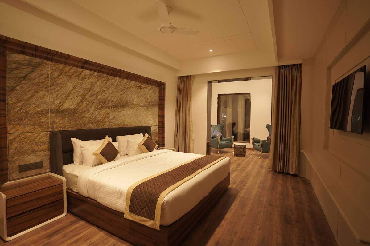 Une chambre d’hôtel moderne dotée d’un grand lit, d’un parquet, d’un mur décoratif en marbre, d’un téléviseur à écran plat et d’un coin salon avec un fauteuil et une petite table.