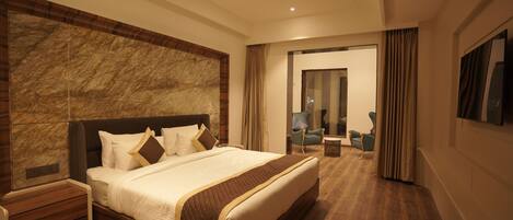Een moderne hotelkamer met een groot bed, houten vloeren, een accentmuur van marmer, een flatscreen-tv en een zithoek met een stoel en een klein tafeltje.