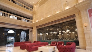 Un lobby lujoso con sofás tapizados en rojo, una mesa de centro blanca y un amplio ventanal con candelabros.