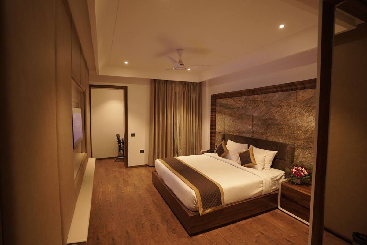Une chambre d’hôtel moderne dotée d’un grand lit, d’un plancher en bois, d’un ventilateur de plafond et d’une table de chevet ornée d’un vase de fleurs.
