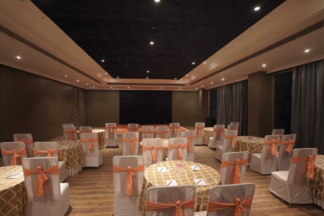 Un salón de banquetes con mesas redondas y sillas, cada una decorada con cintas naranjas.