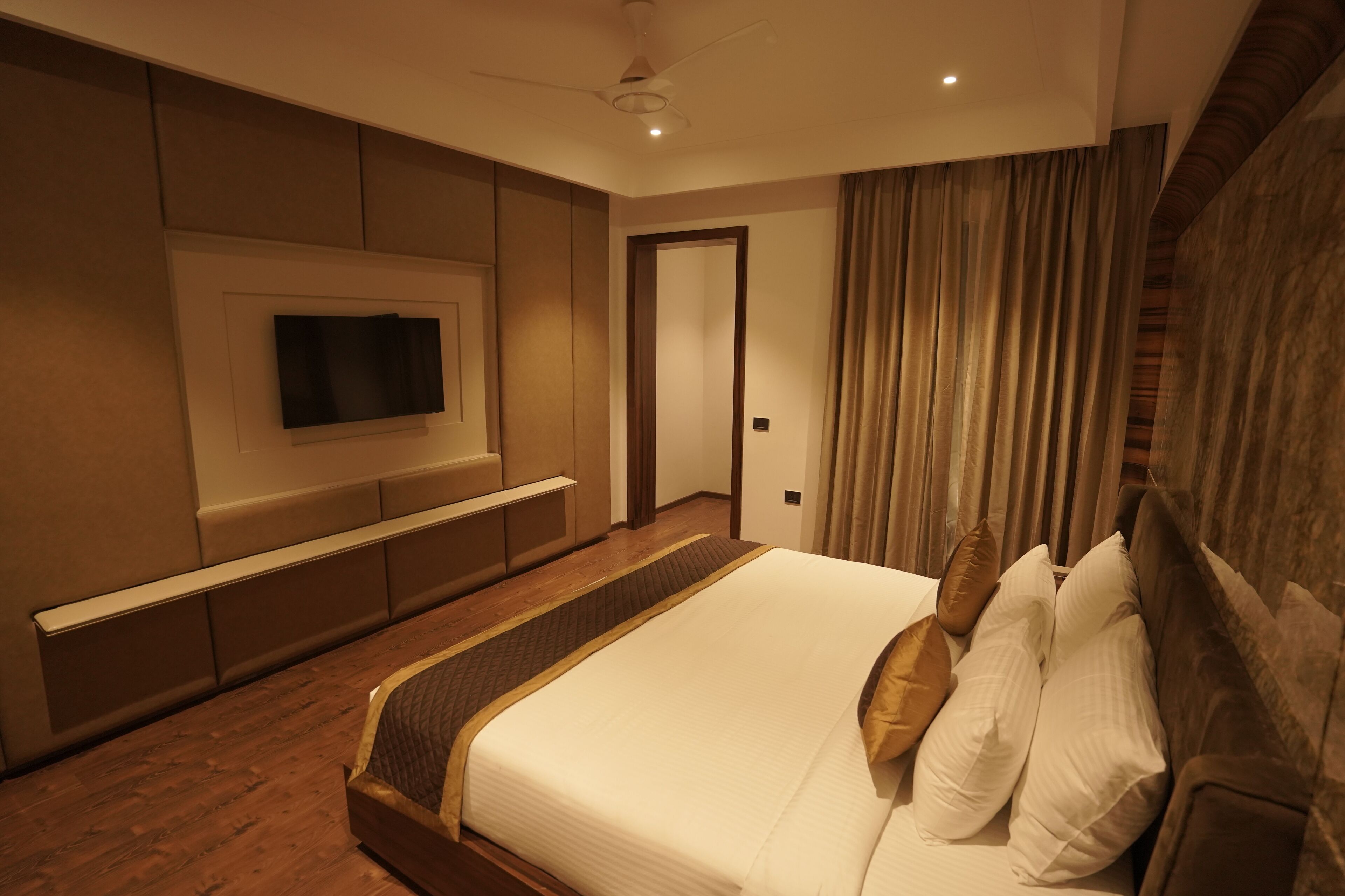 Una habitación de hotel moderna con una cama grande, un televisor de pantalla plana en la pared y un ventilador de techo.