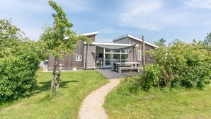 Une maison moderne dotée d’un patio couvert, d’un chemin de gravier menant à l’entrée et entourée de verdure.