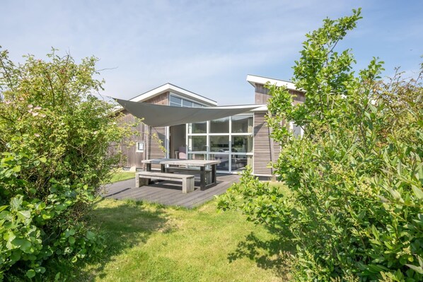 Une maison moderne dotée d’un patio, de grandes fenêtres et d’une terrasse en bois.