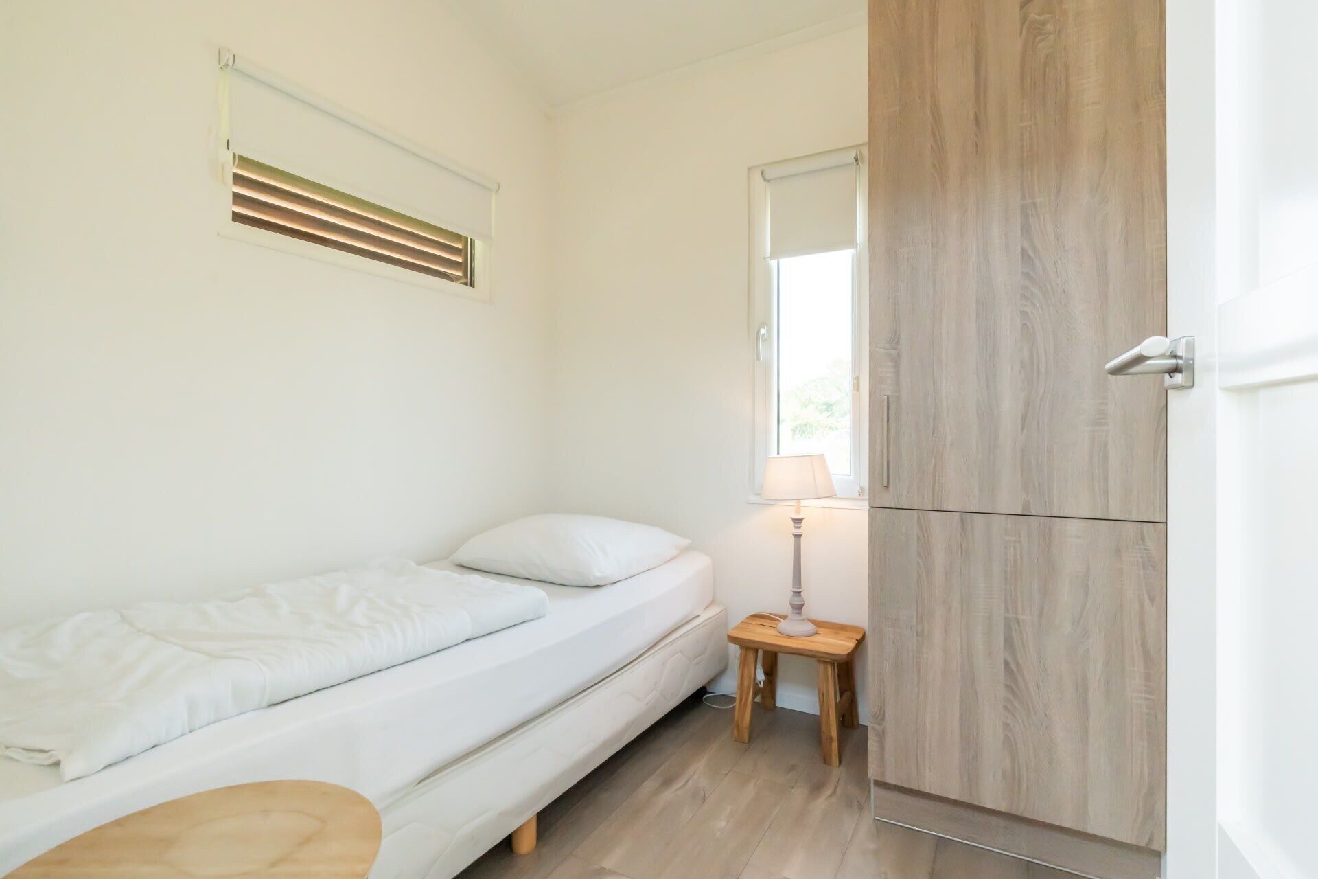 Une petite chambre propre, avec un lit, une table de chevet, une lampe et une armoire.