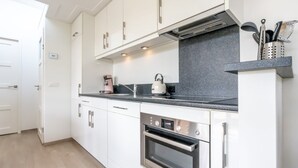 Une cuisine moderne avec des meubles blancs, un four Bosch, une machine à café et une bouilloire posée sur le plan de travail.