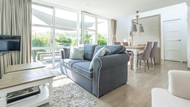 Un salon moderne avec un canapé gris, un téléviseur à écran plat et un coin repas comprenant une table et des chaises.