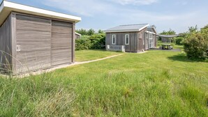 Un bâtiment moderne doté d’un grand portail de garage, d’un patio couvert et d’une cour gazonnée.