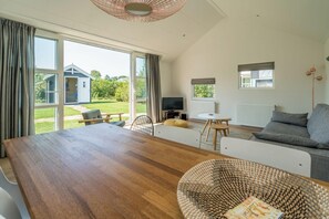 Un vaste espace de vie comprenant une grande table en bois, un canapé gris et un téléviseur.