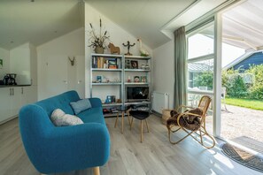 Un salon moderne avec un canapé bleu, une bibliothèque, un téléviseur et un fauteuil en osier.