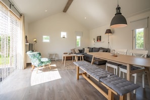 A spacious living area with a dining table, benches, a sofa, and a large window providing natural light.