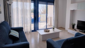 A modern living room with a sofa, a coffee table, and a TV. There is a sliding glass door leading to an outdoor area.
