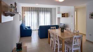 A modern living room with a sofa, a dining table with chairs, and a kitchen area in the background.