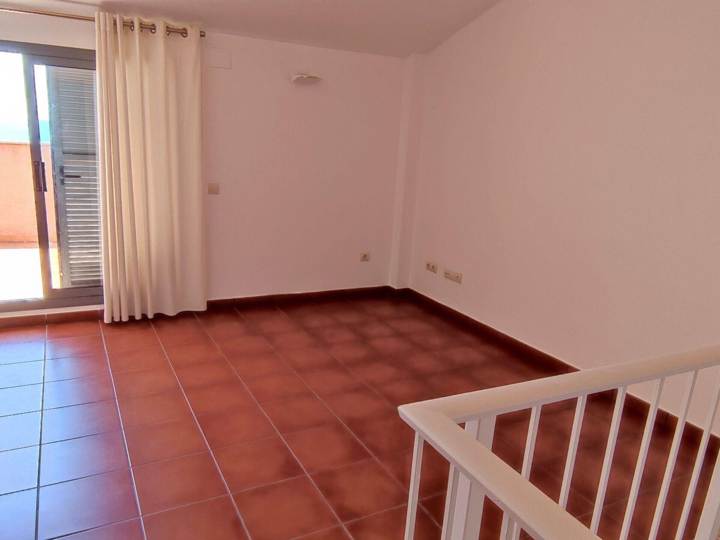 Una habitación con suelo de baldosas, barandilla blanca y ventana con cortina.