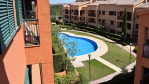 A view of a swimming pool surrounded by well-maintained lawns and a multi-story building with balconies.