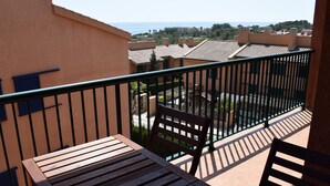 A balcony with a wooden table and chairs, overlooking a residential area with houses and a view of the sea.