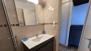 A modern bathroom with a white sink, dark cabinets, a mirror, and a shower area. - Charming Studio with Pool, Balcony, and Central Location for 2 in Agde (Cap d'Agde)