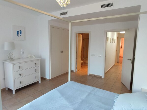 Une chambre à coucher avec un lit, une commode et un espace douche visible à travers une porte ouverte.