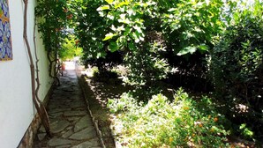 A stone pathway leading through a lush garden with dense foliage and flowering plants. - Charming Rustic Villa with Pool & Mediterranean Garden (L'Ametlla de Mar)