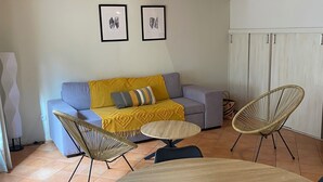 Un salon chaleureux avec un plafond en bois, un canapé agrémenté d’un plaid jaune, deux tableaux encadrés et une table ronde en bois.