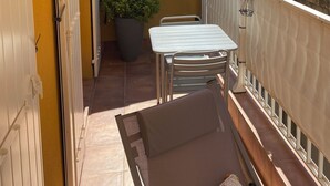Un petit balcon avec une table et des chaises blanches, une plante en pot, et une vue sur un bâtiment historique en arrière-plan.