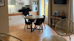 Une cuisine chaleureuse avec des poutres apparentes en bois au plafond, une table à manger avec des chaises et un téléviseur fixé au mur.