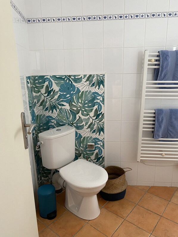 Ein Badezimmer mit Toilette, einem blauen Mülleimer und einem Handtuchhalter mit Handtüchern.