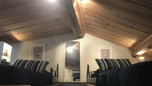 Une chambre confortable située sous les toits, avec des poutres en bois, un mur miroir et deux lits dotés d’oreillers à rayures.