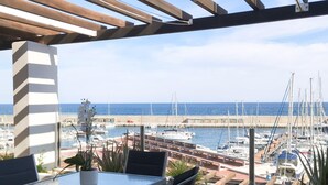 Una terraza con mesa y sillas, con vistas a un puerto deportivo y barcos.
