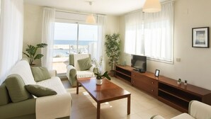 Una sala de estar moderna con un sofá, una mesa de centro, un televisor sobre un mueble de madera y un balcón con vistas al mar.