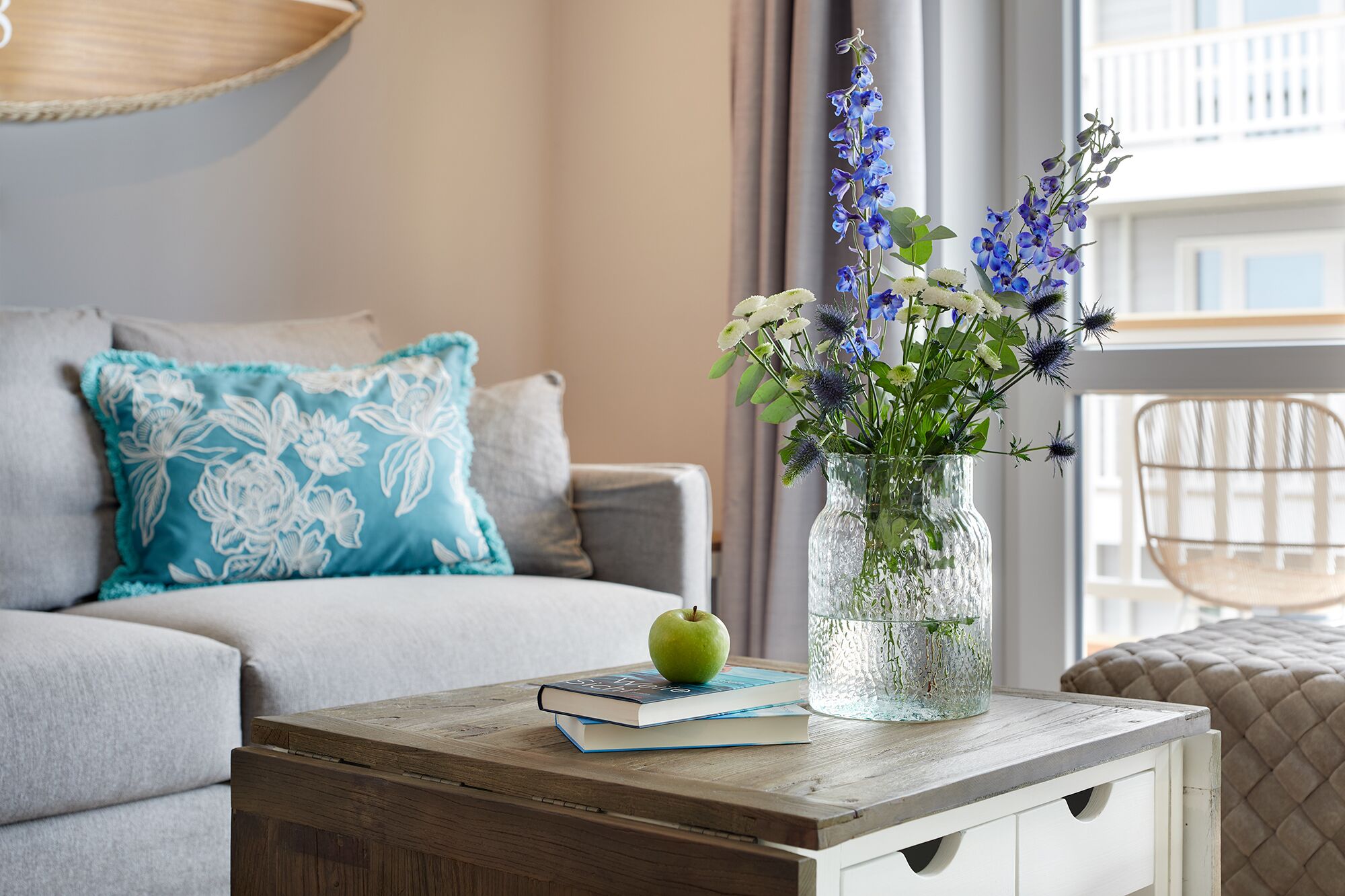 A living room with a sofa, a coffee table with a book and an apple, and a vase with flowers.