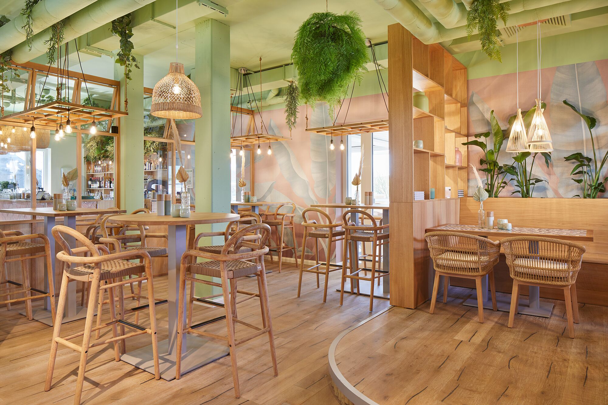 A restaurant interior with wooden furniture, hanging plants, and a bar area.