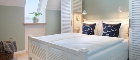 A bedroom with a bed, a window, a bedside table, a lamp, and a wall-mounted shelf.