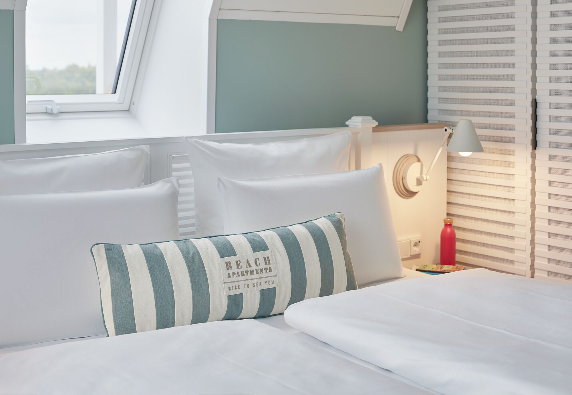 A neatly made bed with white linens, a striped pillow, and a bedside lamp.