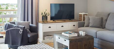 A modern living room with a grey sofa, a matching armchair, a wooden coffee table, and a flat-screen TV on a white cabinet.