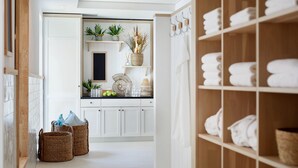 A hallway with a kitchen area, featuring white cabinets, a blackboard, and a shelf with towels. - Beach Apartments Büsum (Büsum)