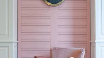 A pink wall with a round clock, a pink chair, and a small table with a book.